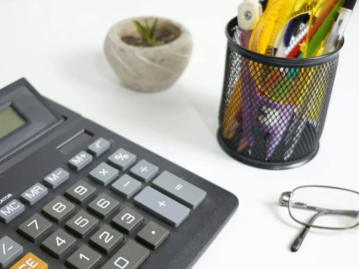 A calculator, glasses and pens on a desk